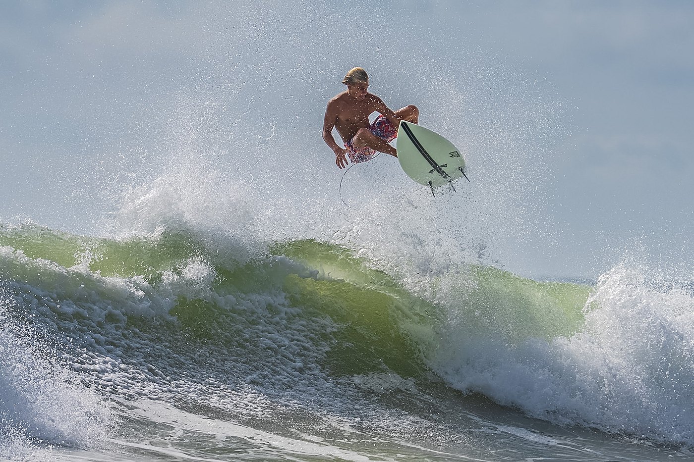 Surfer in mid-air above the wave lip during an aerial