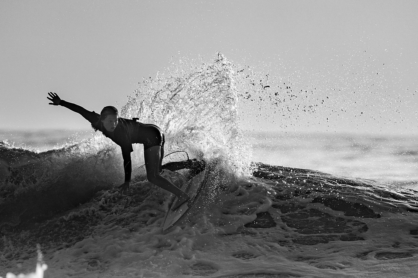 Black and white photo of a surfer carving through backlit spray