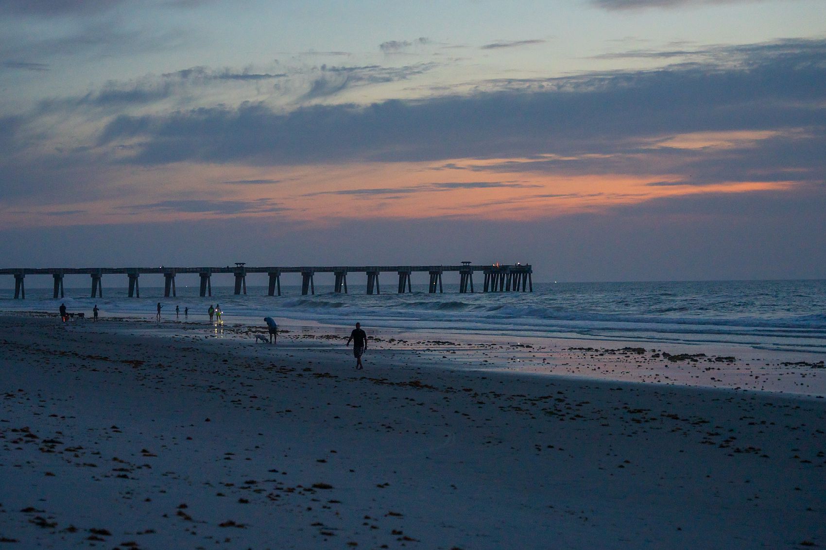 The pier at first light as people walk the shoreline