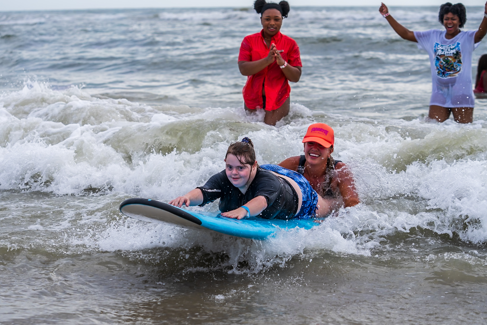 A young athlete in noise-canceling headphones rides the whitewater at a Surfers for Autism event, a volunteer close behind