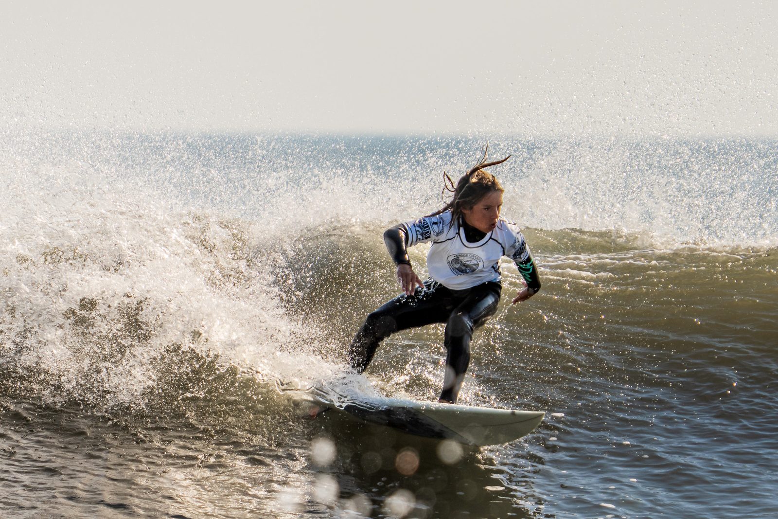 Young surfer riding backlit with hair and spray flying