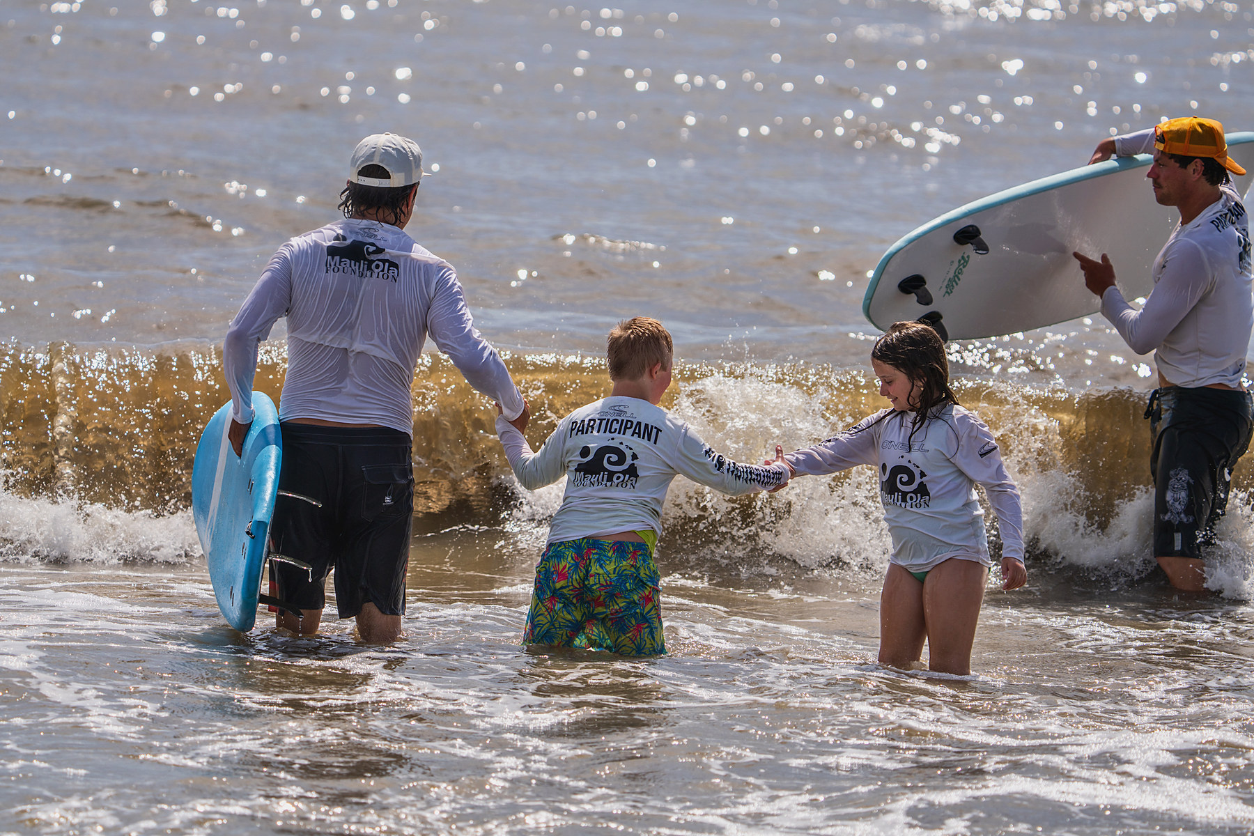 Hand to hand through the shorebreak. The volunteer on the left carries the board so the participants can concentrate on the footing.