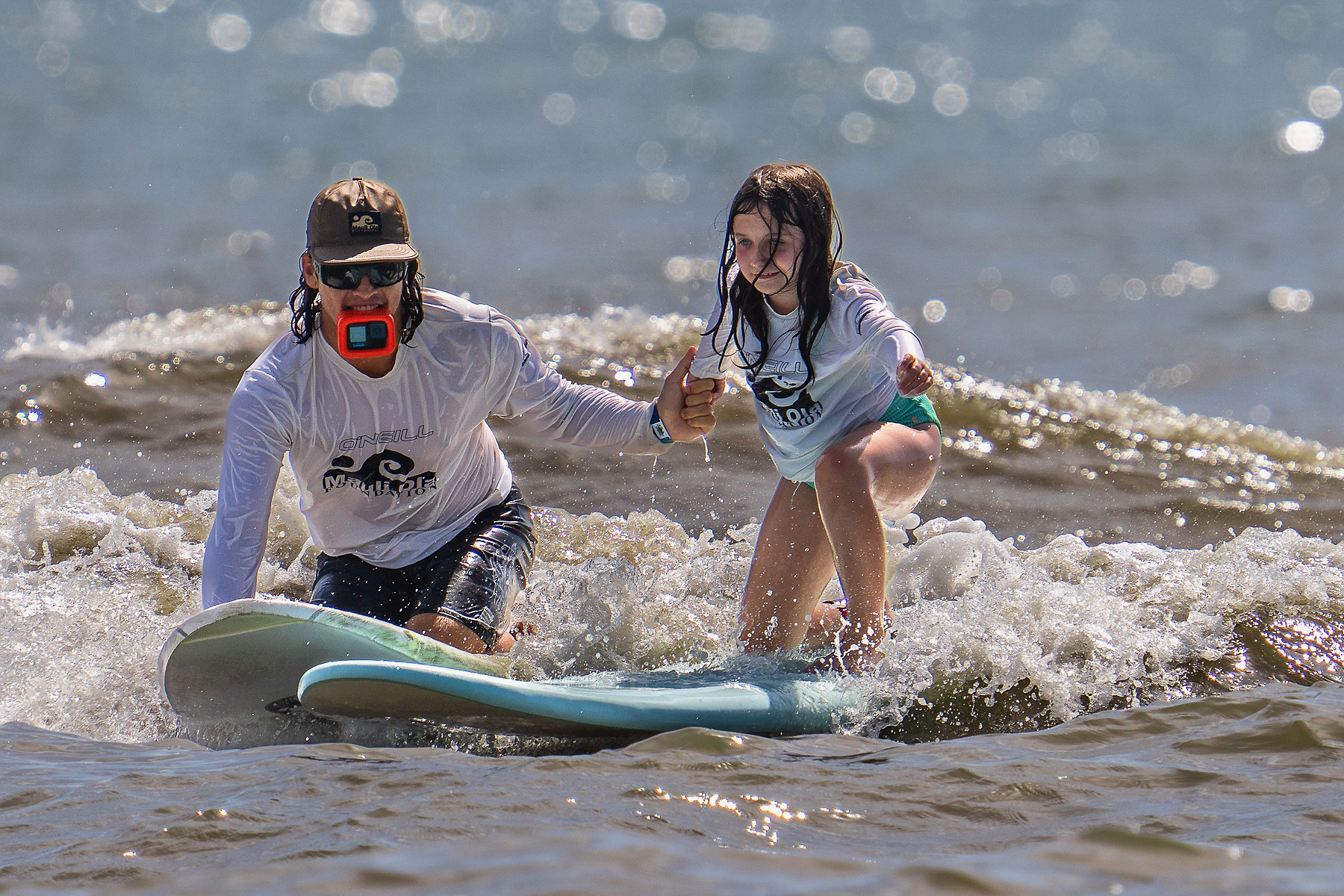 A volunteer rides in alongside a surfer with a camera in his teeth, so the family goes home with footage from the water.