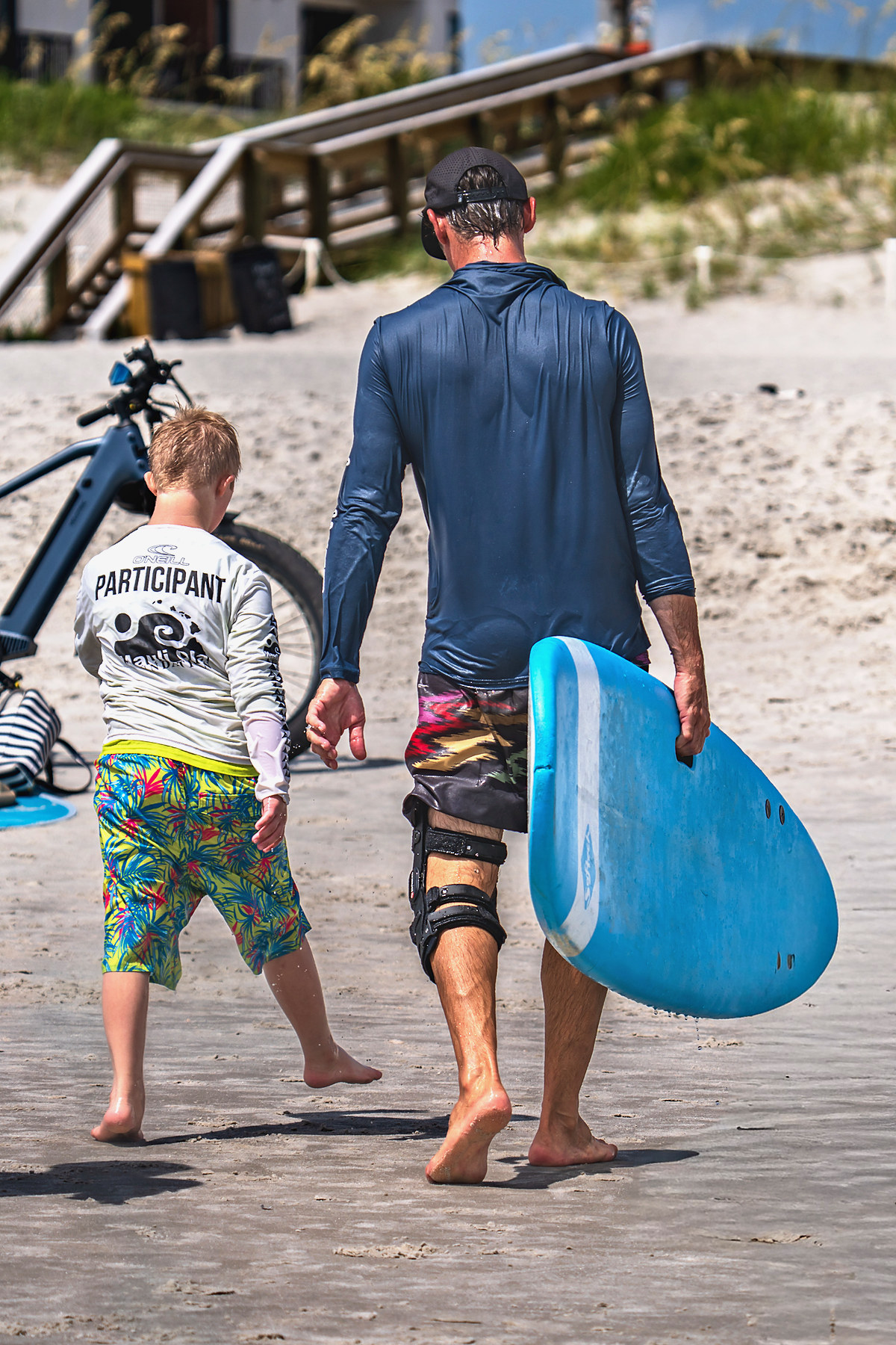 A volunteer walks a participant back up to the tents. He surfed the morning in a knee brace.