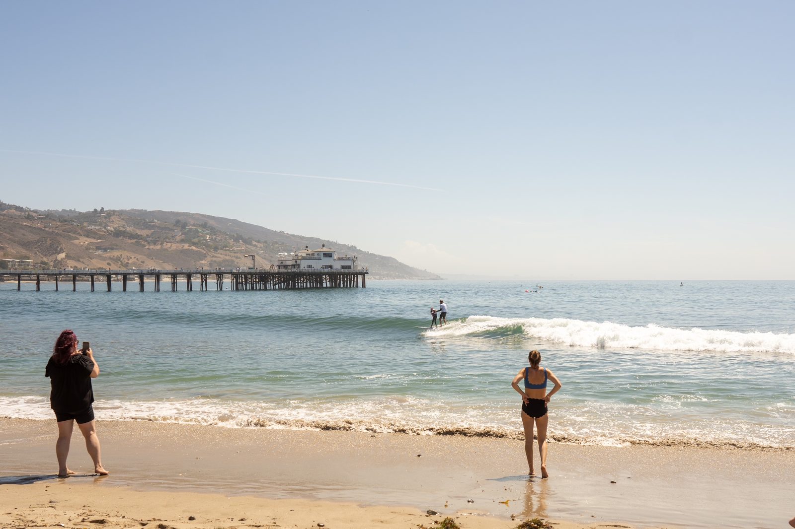 Hans Hagen and Maddie riding a wave together near the Malibu Pier while her mother watches from the beach