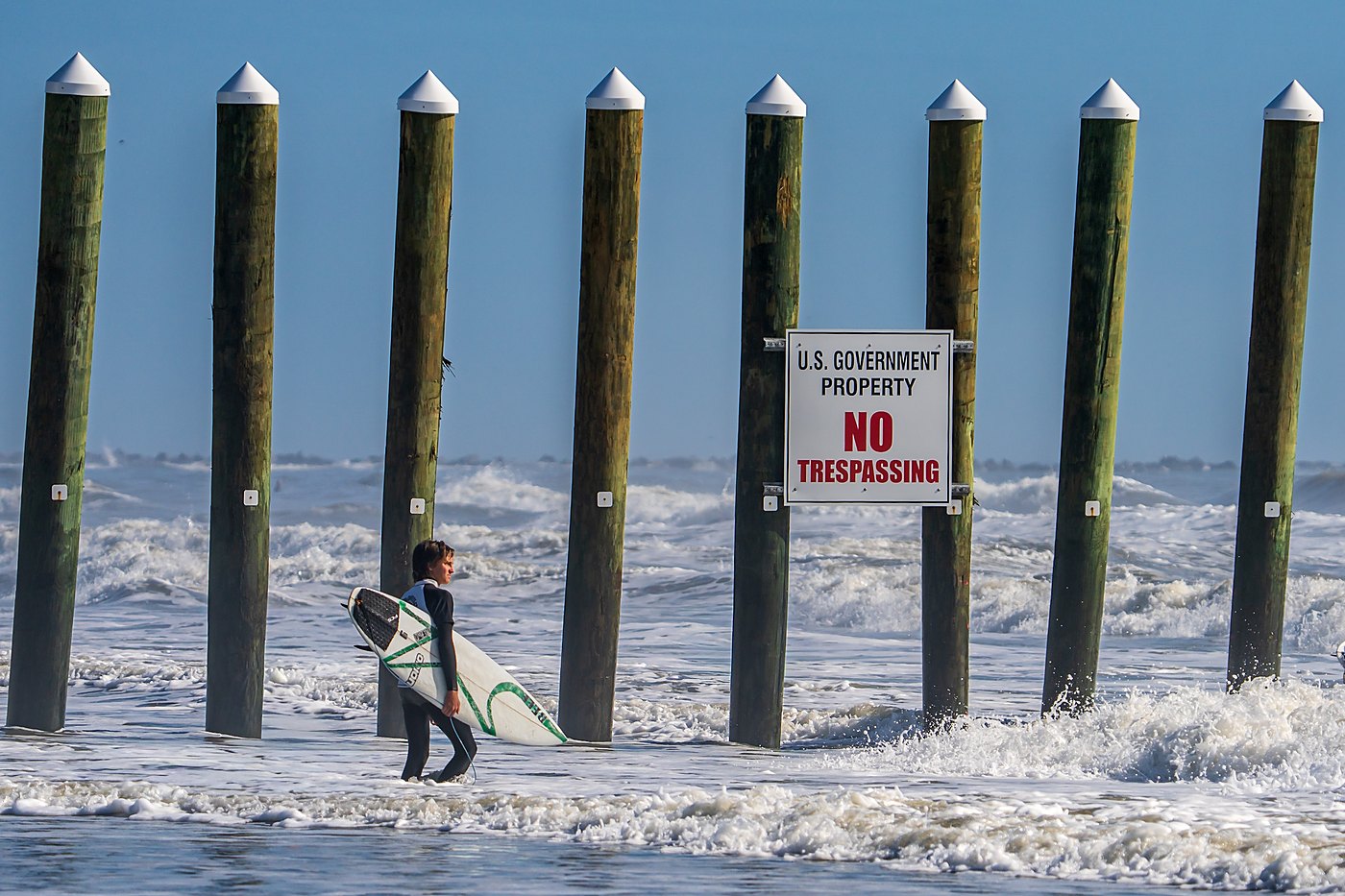 Surfer walking beside pilings and a no trespassing sign