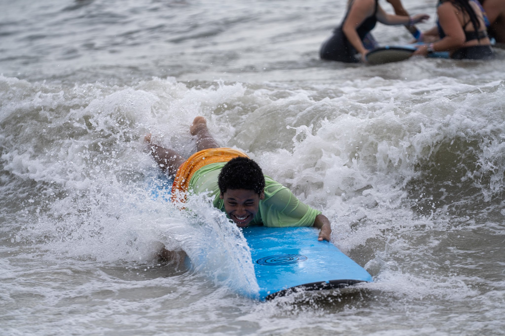 A young athlete in noise-canceling headphones rides the whitewater at a Surfers for Autism event, a volunteer close behind