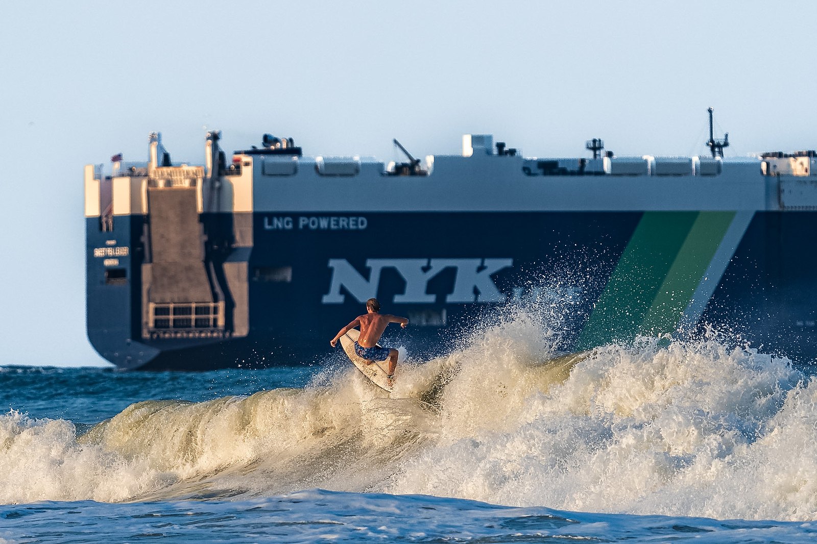 A lone surfer rides a wave as a cargo ship passes offshore on Florida's First Coast