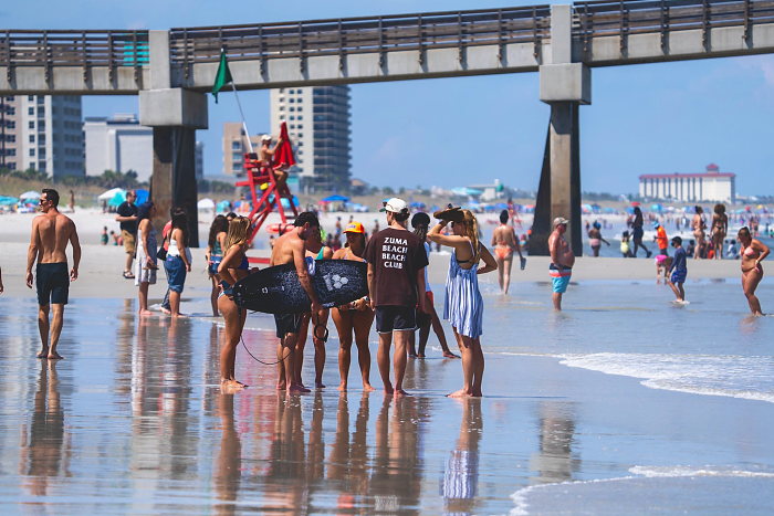 Competitors and spectators gather at the waterline with the Jacksonville Beach Pier behind them.