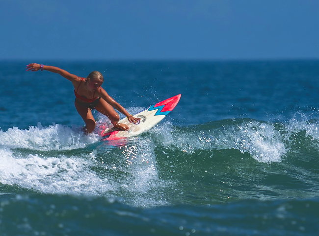 A surfer carves off the top of a wave, arms extended.